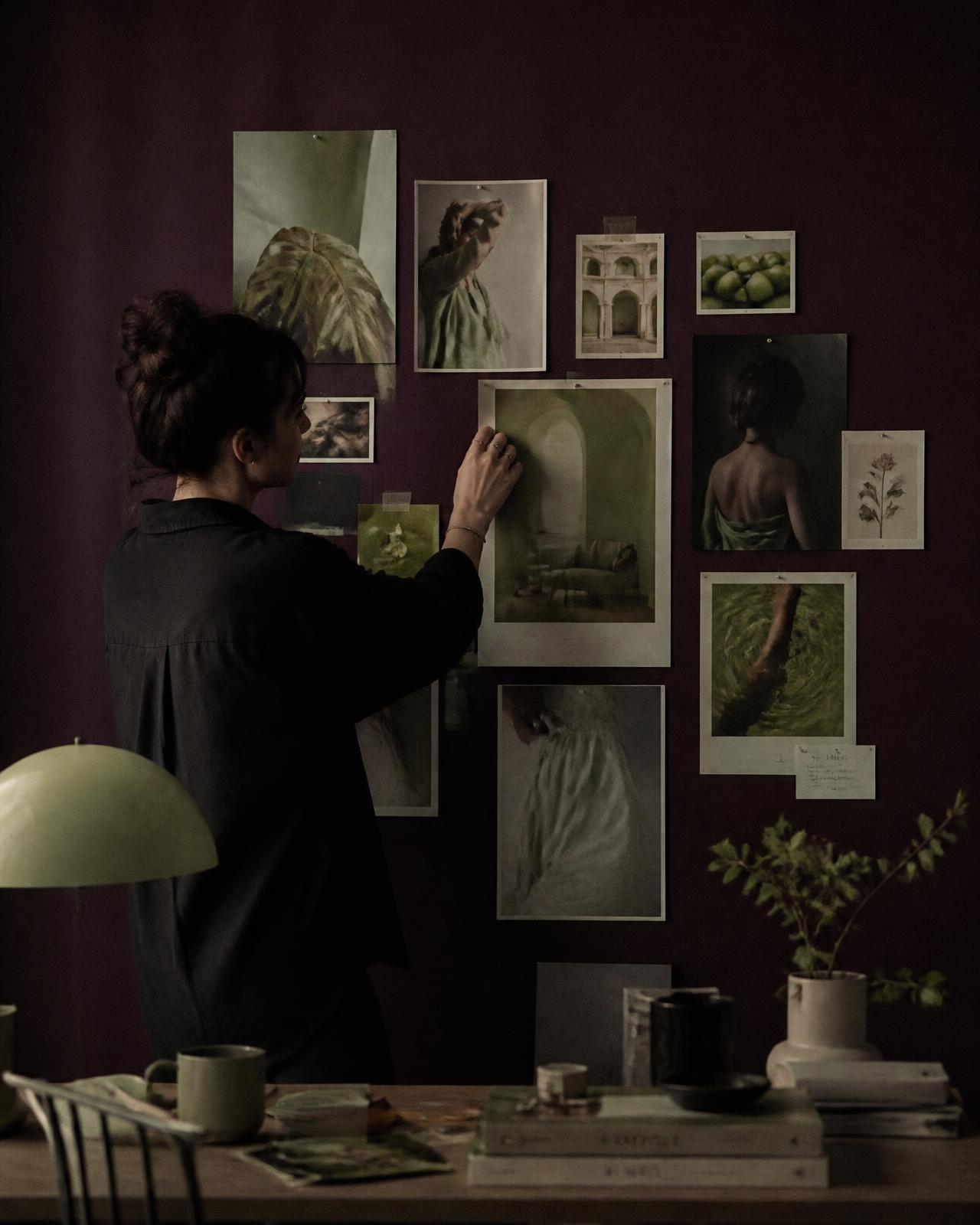 Art director som sätter upp referensbilder på en djup plommonfärgad moodboardvägg